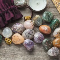 Elder Futhark Rune Stones Set Made of Natural Gemstones, Sage Incense, Candle, Old Book on Wooden Background